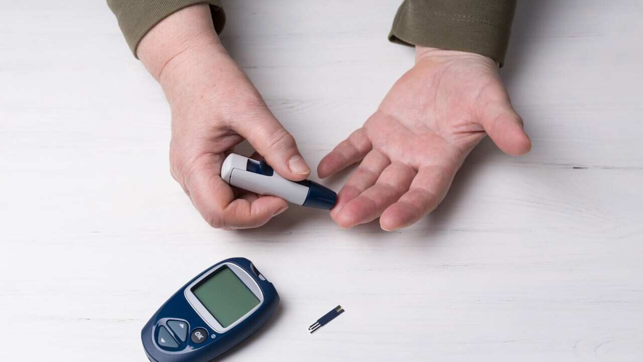 A close-up macro plan. Hands of a adult woman on a light wooden background or table. It uses the technology of an instrument for measuring the level of glucose in the blood.