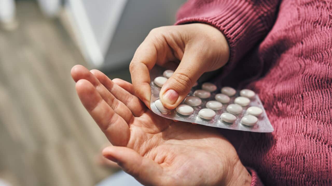 A person's hands popping white pills out of a blister pack.