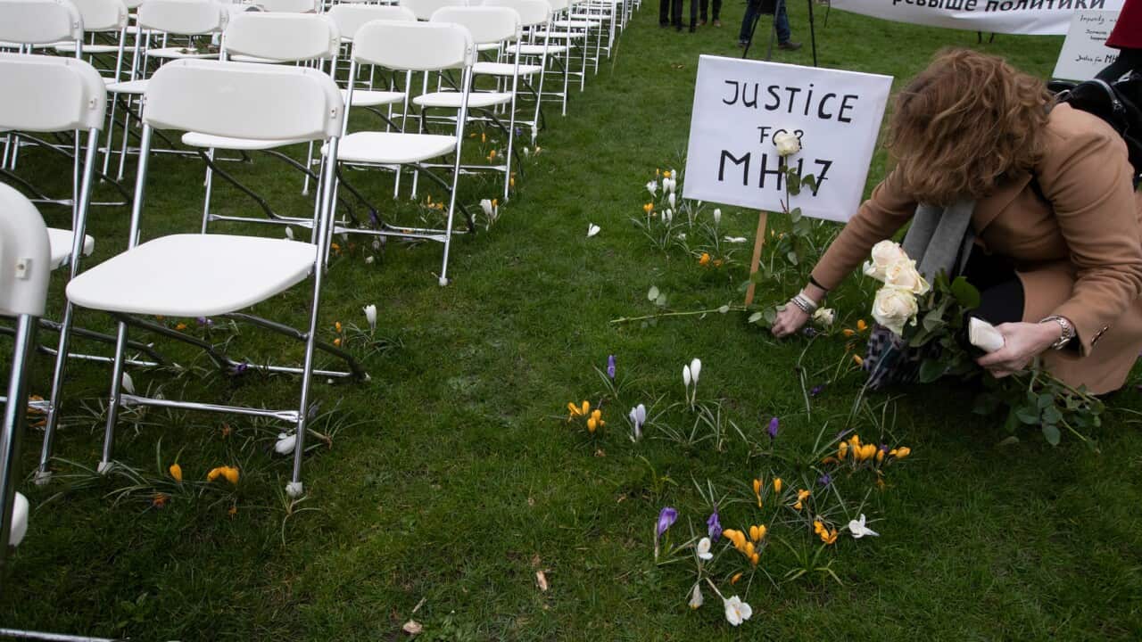 A woman places a rose next to 298 empty chairs, representing the victims of the MH17 crash