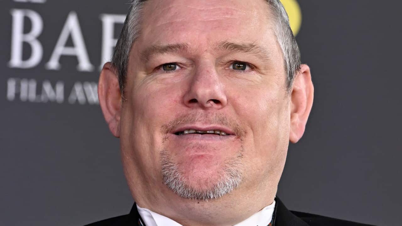 A head-and-shoulders shot of a man in a suit looking at the cameras with a slight smile on his face.