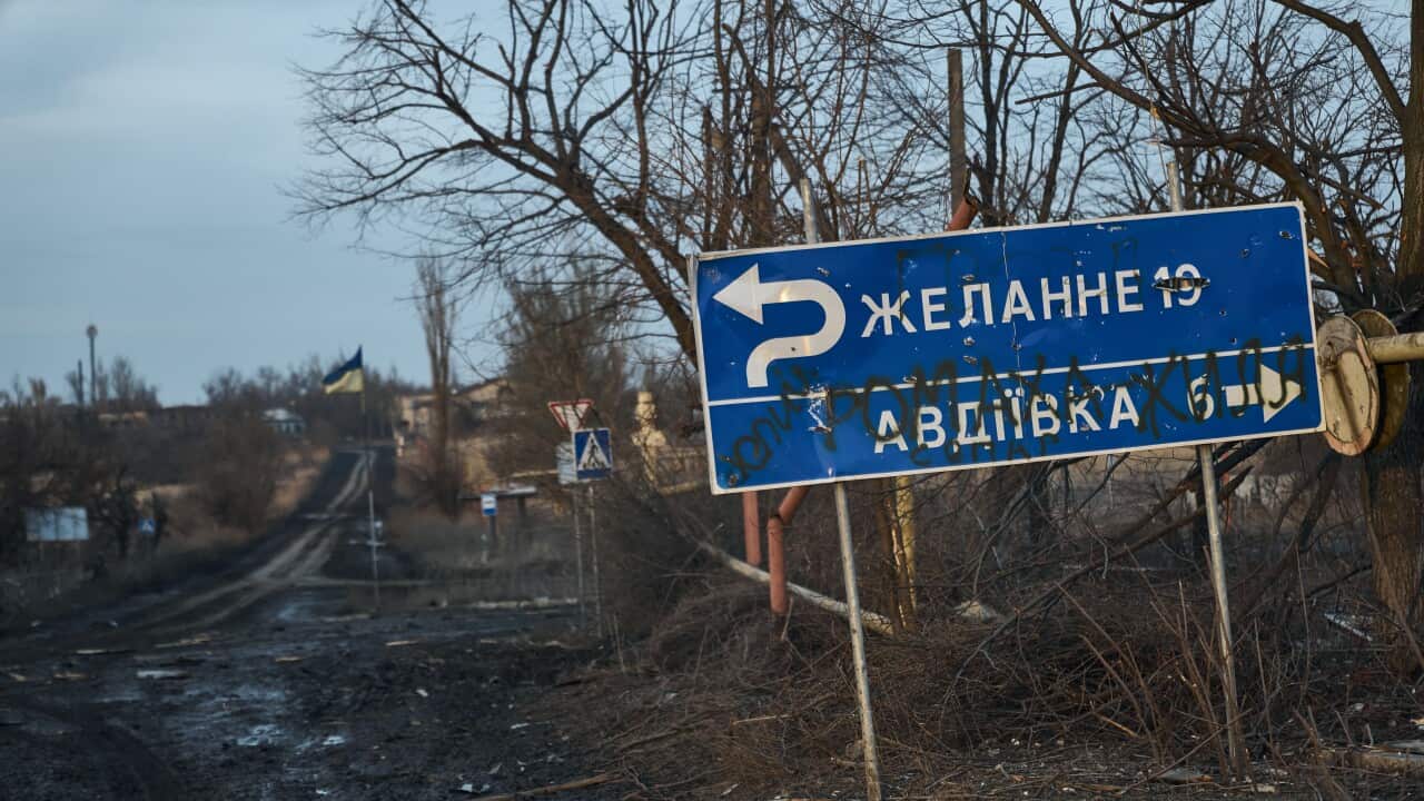 A battered street sign on the outskirts of Avdiivka, next to a muddy road and a roadside littered with debris.