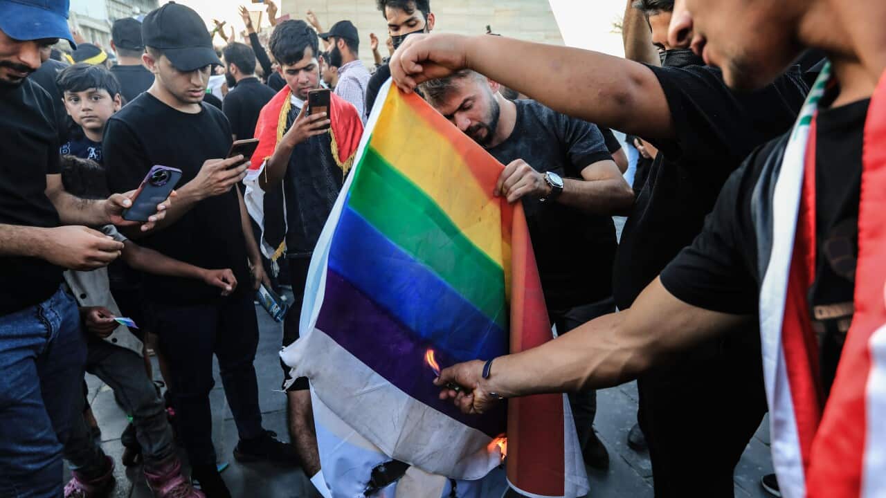 A group of men lighting a rainbow flag on fire