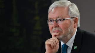 An older white man with grey hair and a short beard, wearing glasses and a suit. He has his right hand up to his chin.