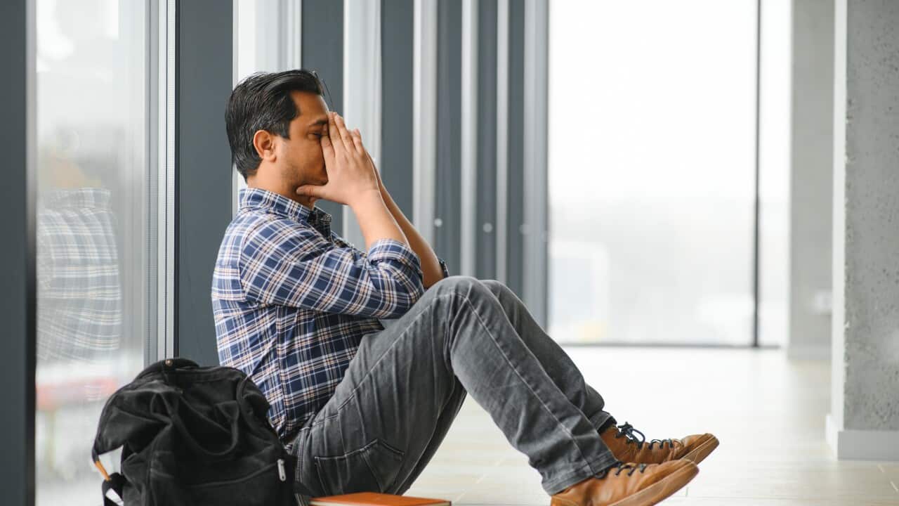 Full length of depressed boy sitting with backpack in school corridor