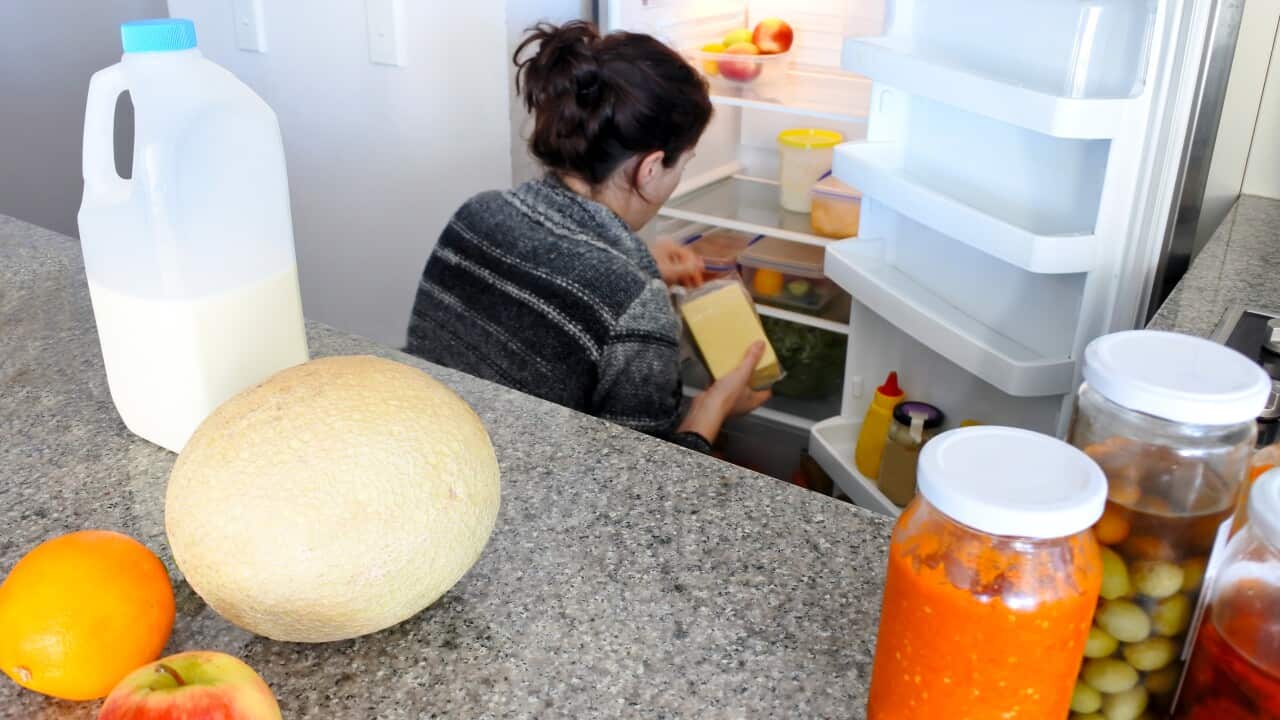 A woman cleaning a refrigerator with fruits, milk and pickle jars places on the kitchen island in the foreground.