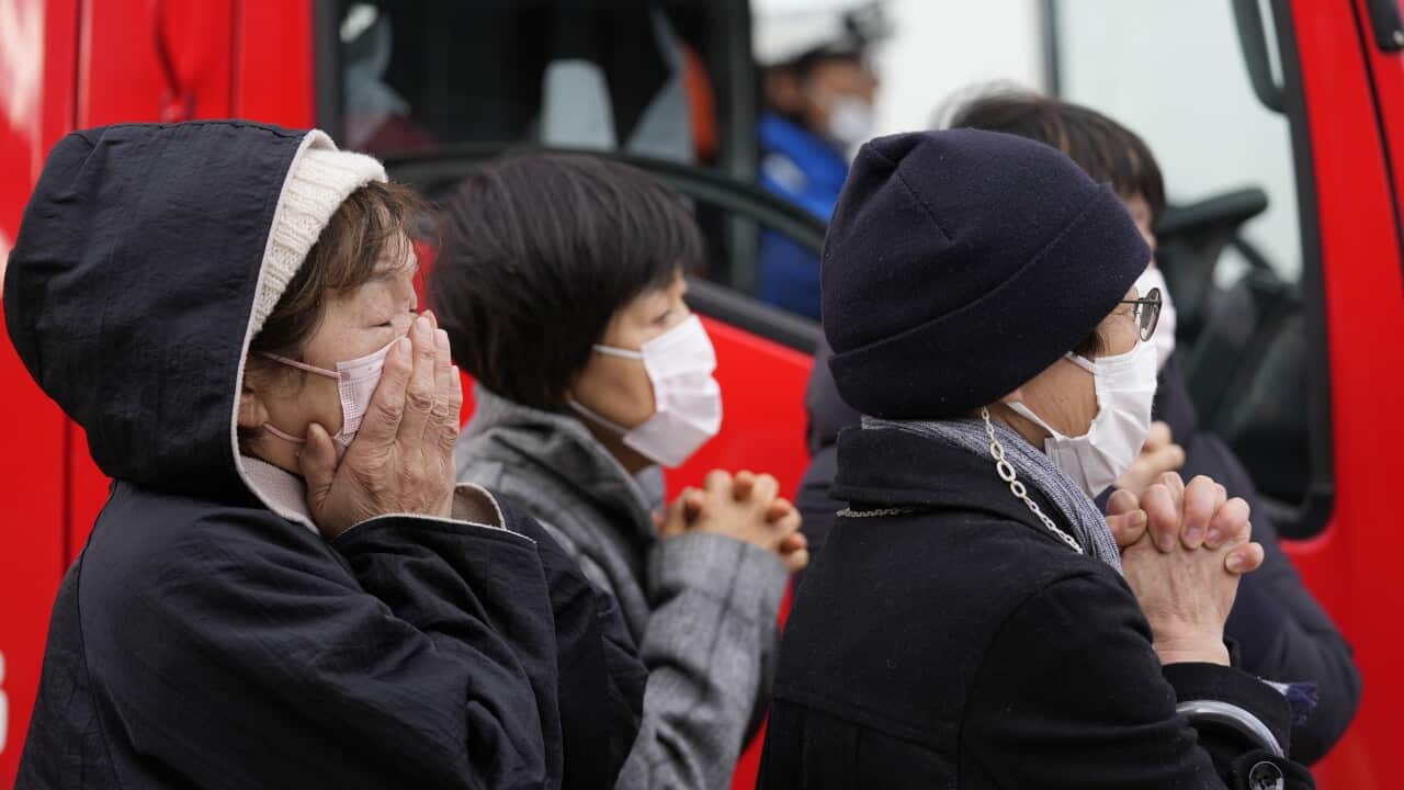 A group of people in winterwear and face masks clasp their hands.