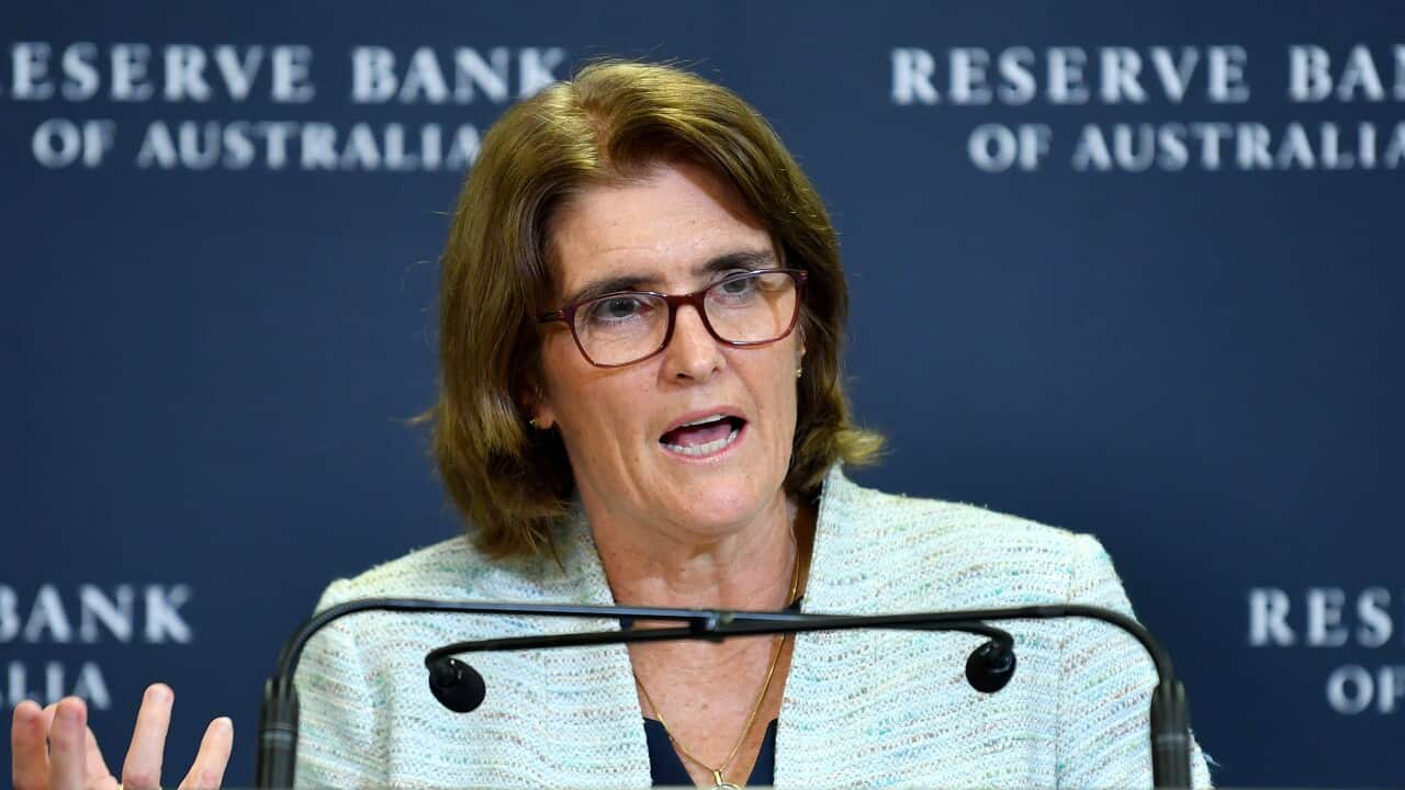 A woman with brown hair standing at a lecture in front of navy background with the Reserve Bank of Australia logo on it