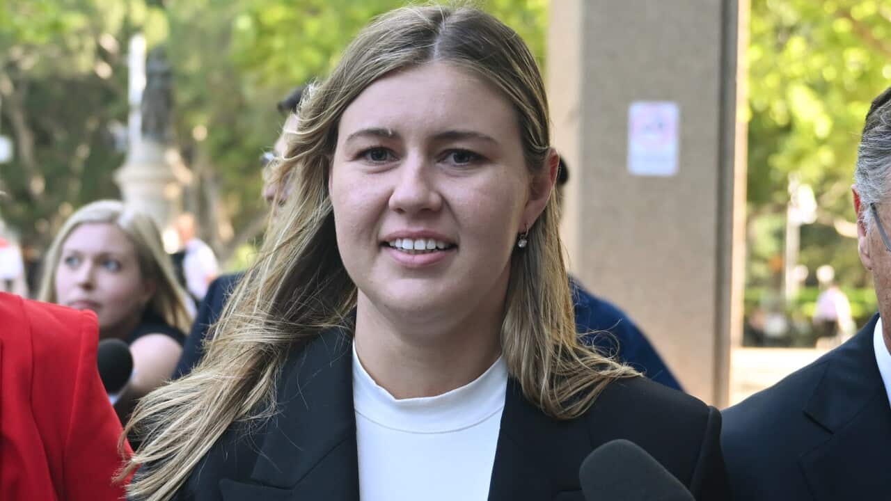 A woman wearing a white top and black blazer walking as a journalist holds a microphone in front of her.