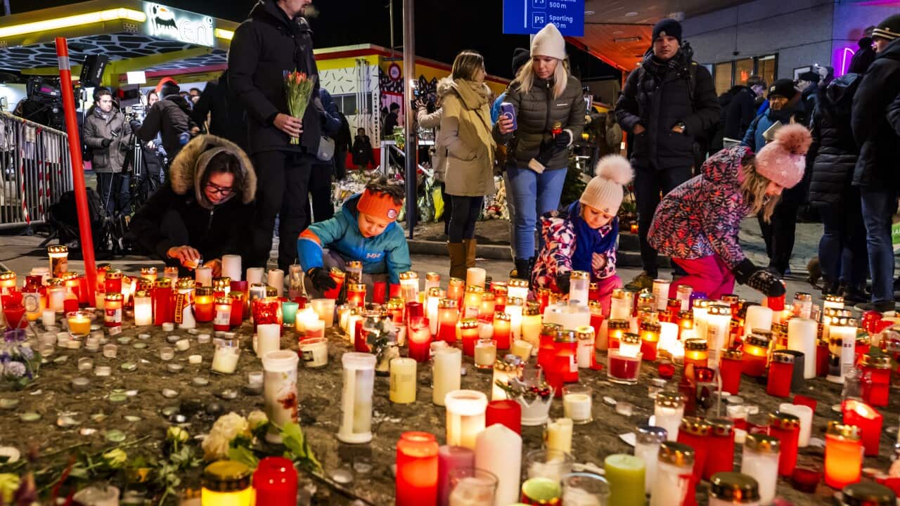A group of people light candles as dozens of candles in front of them burn at night time
