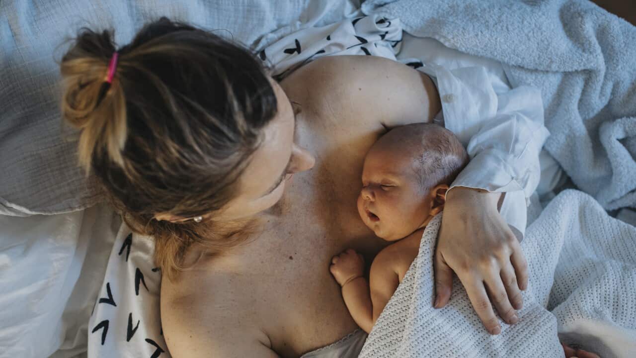 Baby sleeping on mother's chest in bed at home