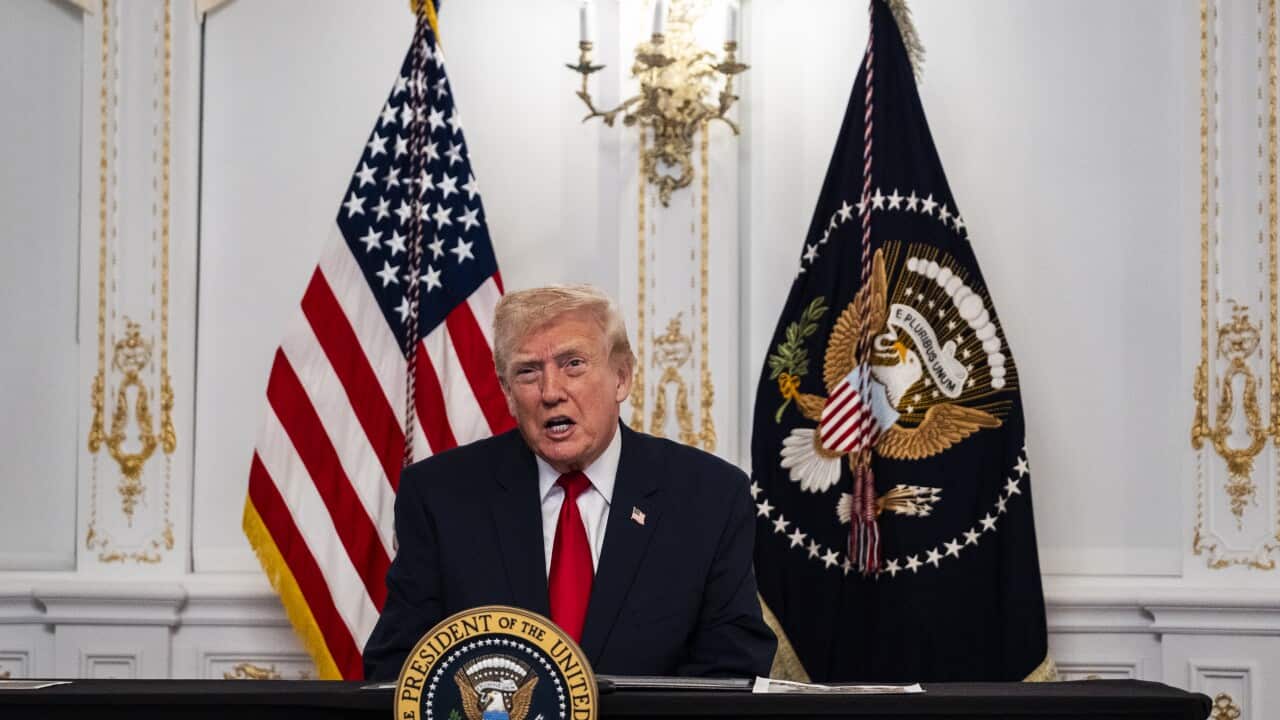 US President Donald Trump addresses US troops on a video call from Mar-A-Lago. He is seated at a table, behind him a US and military flag.