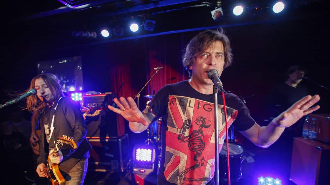 Two  male members of a rock band on stage. One is playing guitar and the other is singing into a microphone on a stand.