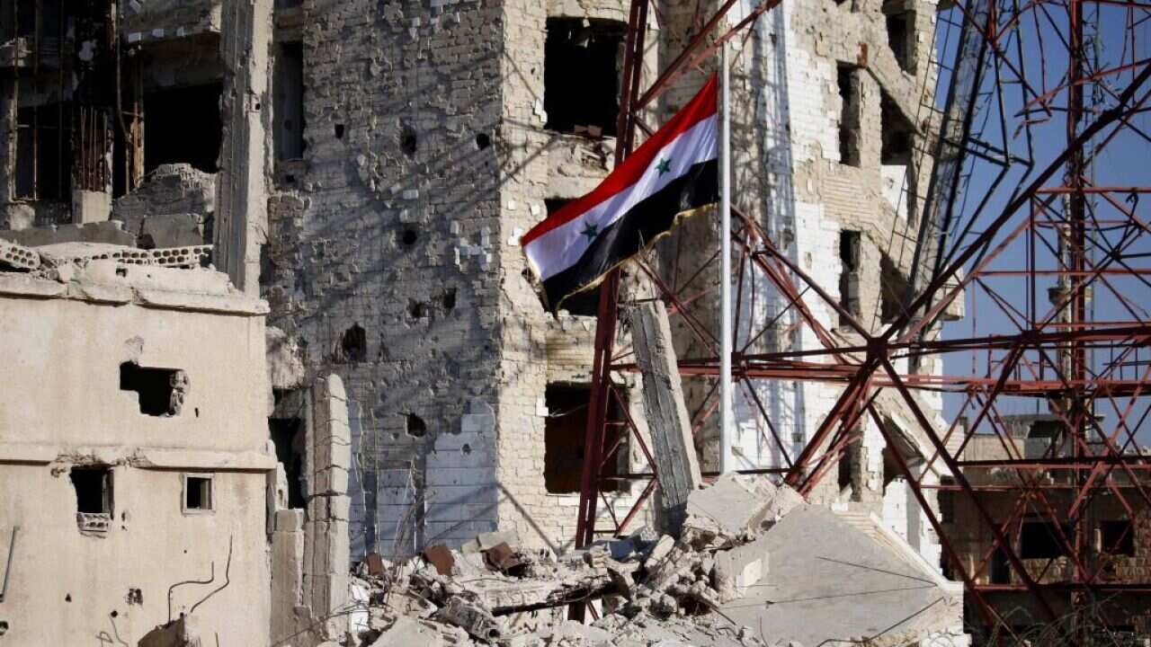 The Syrian national flag rises in the midst of damaged buildings in Daraa-al-Balad, an opposition-held part of the southern city of Daraa, on July 12, 2018.