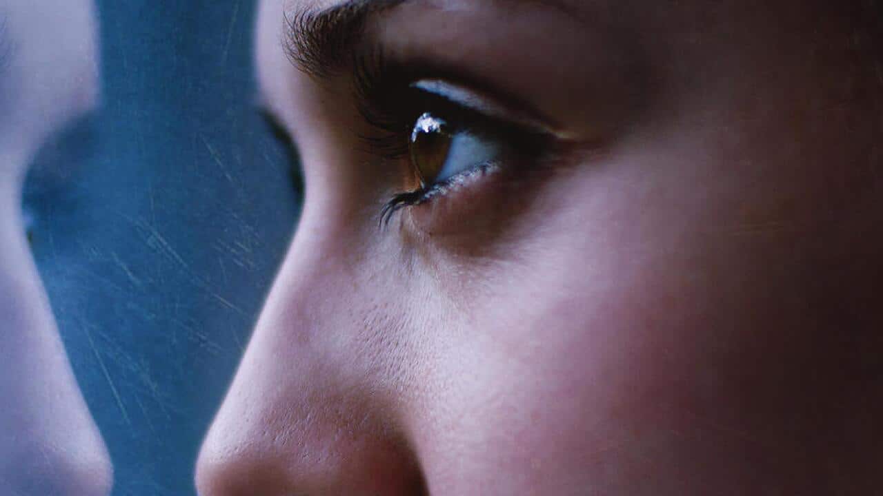 Woman's face close up, staring in mirror with reflection.
