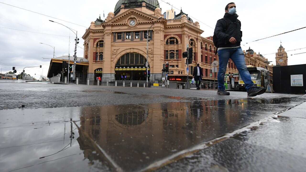 People wearing face masks walk across the road at Flinders Street Station in Melbourne.