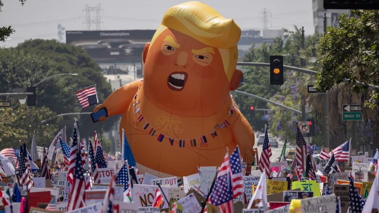 A huge inflatable balloon depicting Donald Trump as an angry baby floats above a dense crowd of protesters holding a multitude of American flags and signs.