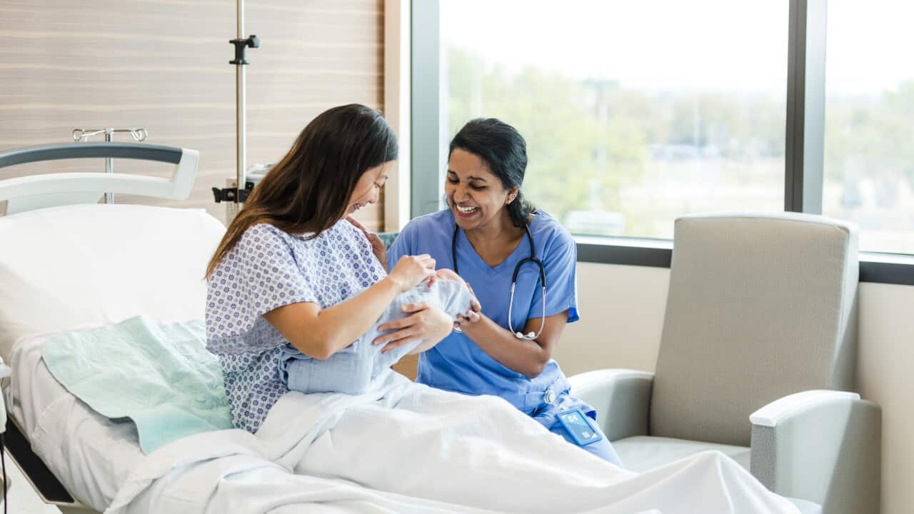 Female nurse smiles while helping reassure the new mother