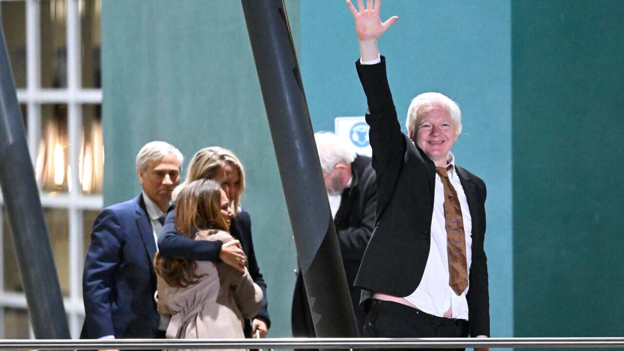 A man in a black suit and white shirt raises one arm above his head