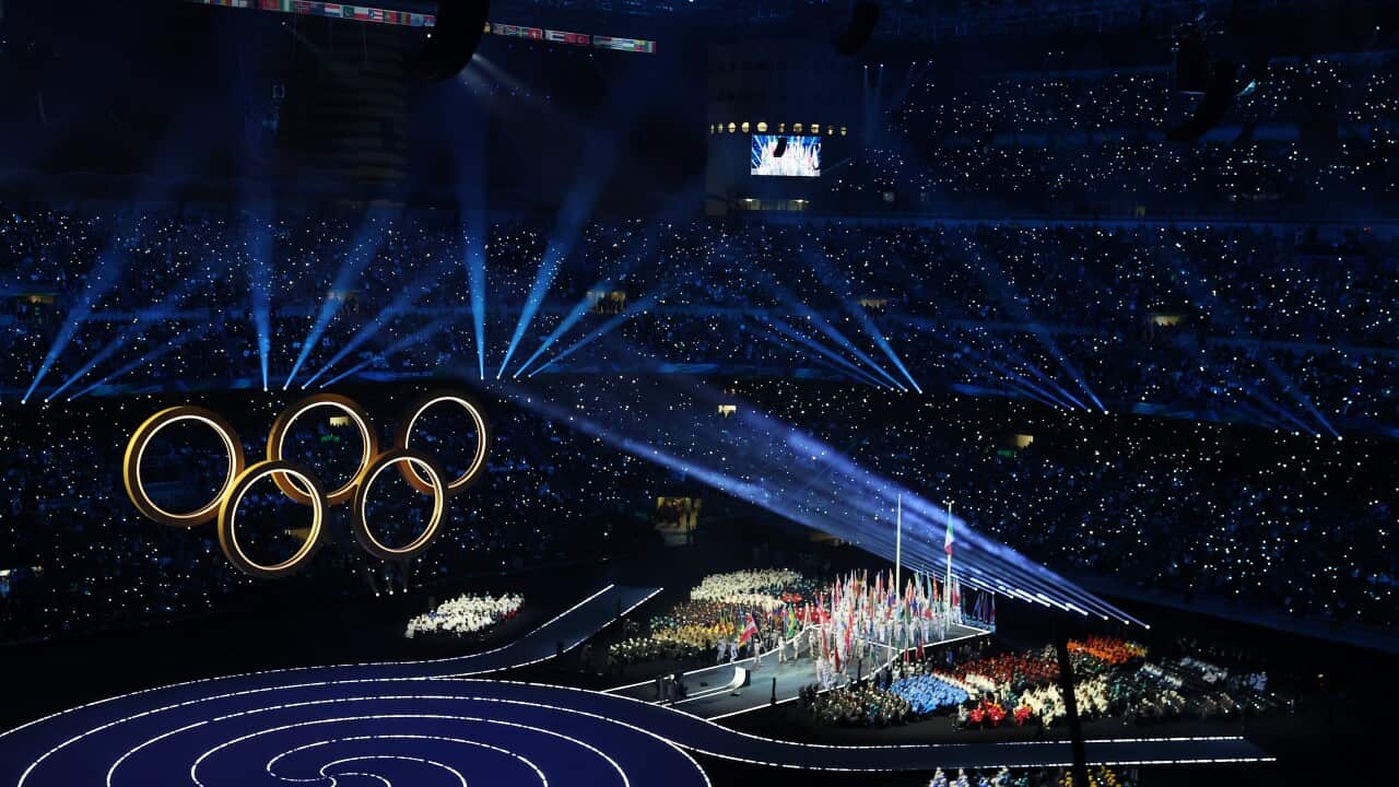The opening ceremony of the Milano Cortina 2026 Winter Olympics, showing large golden Olympic rings over a crowd of people in a large stadium