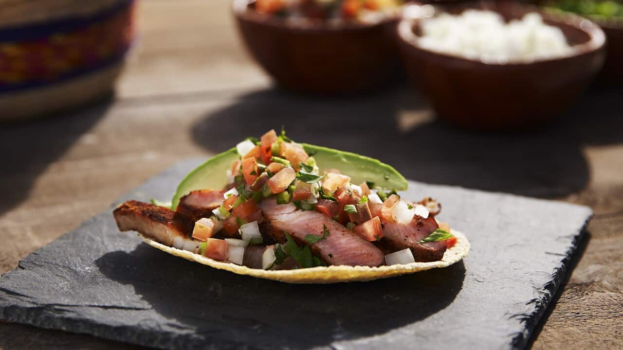 A flat tortilla holds meat, salsa and a slice of avocado.
