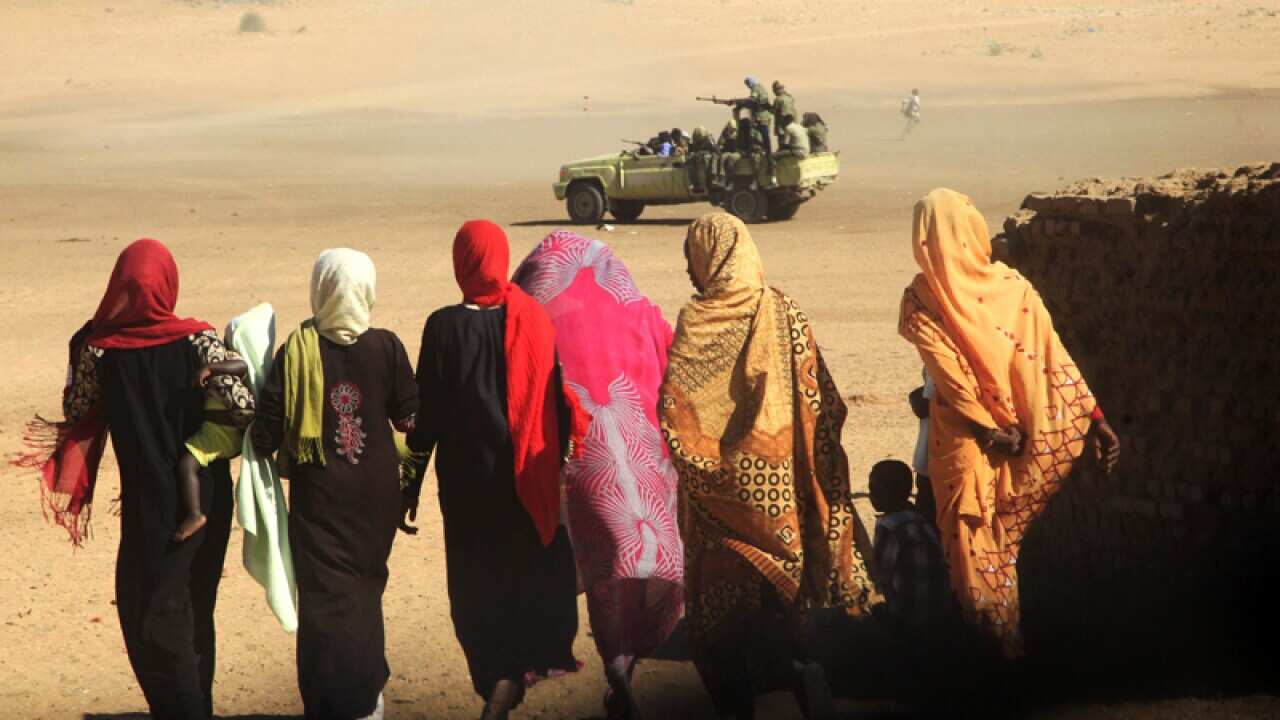 Women and their children walk near a truck carrying government troops