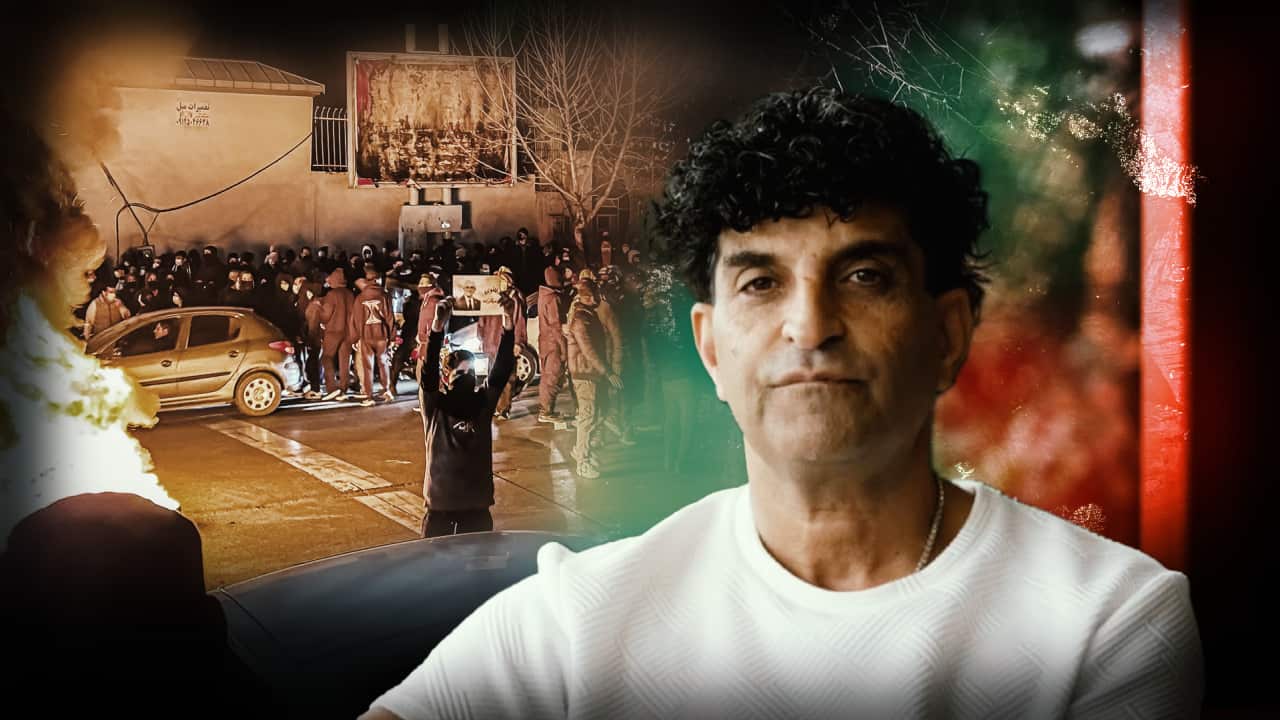 An Iranian man in the foreground, with a nighttime street protest and flames behind him.
