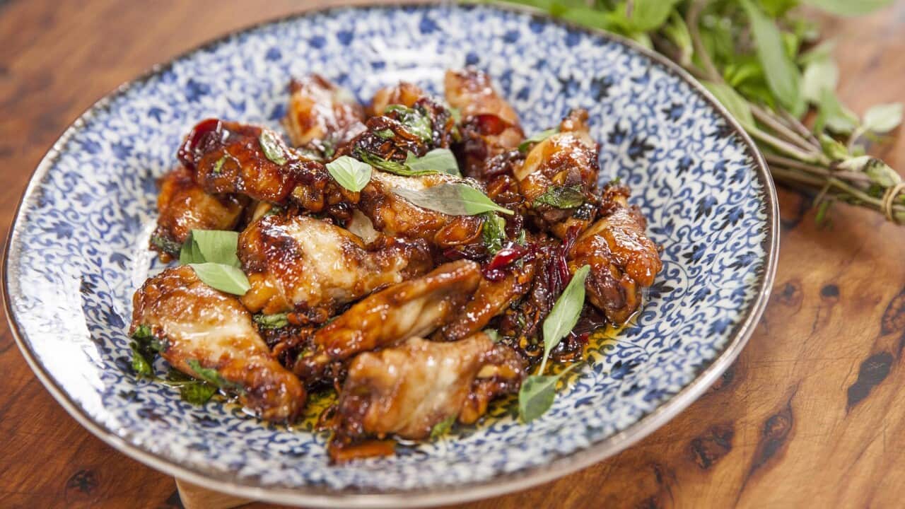 Sticky stif-fried chicken wings sit on a blue-patterned plate, on a wooden surface.