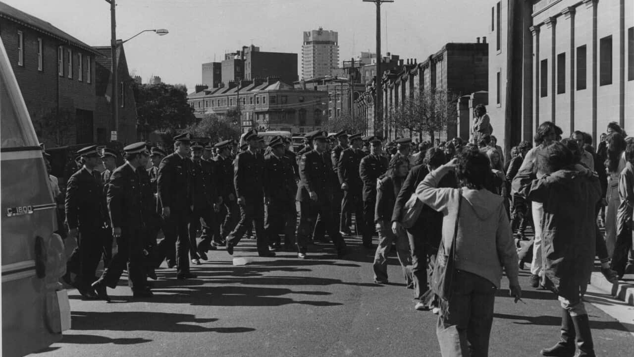 A black and white photo depicting dozens of police officers outside a police station in the 1970s.