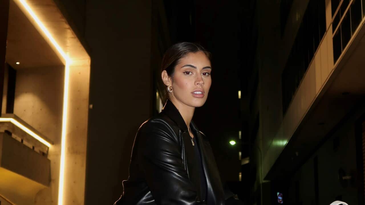 A young woman standing outside in the evening wearing a leather jacket.