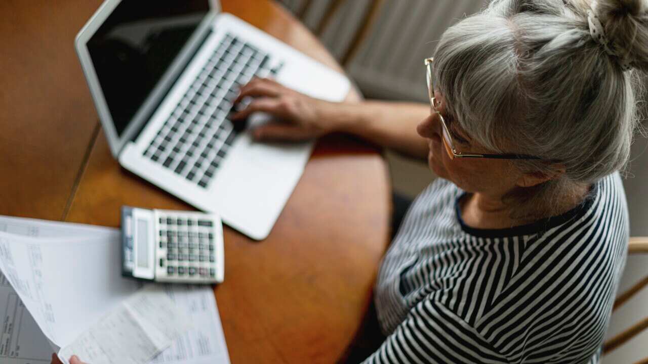 A woman sitting at a table holding papers. A laptop and calculator are also in front of her.