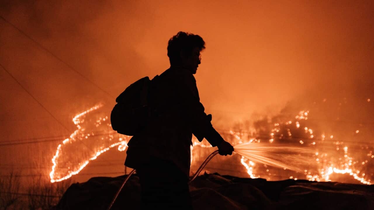 A silhouette of a person spraying a hose with a wildfire in the background.