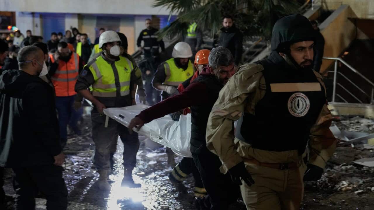 Emergency service workers carry a body bag through building debris