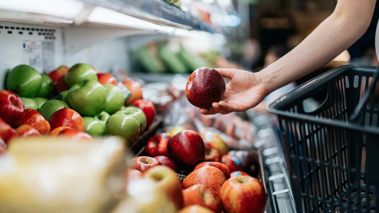 Cropped shot of young Asian woman choosing fresh organic fruits in supermarket. She is picking a red apple along the produce aisle. Routine grocery shopping. Healthy living and eating lifestyle