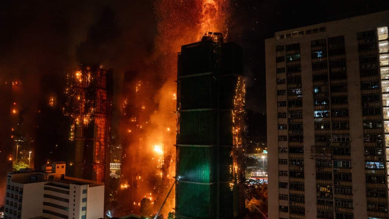 A building complex that has gone up in flames, amid other buildings.
