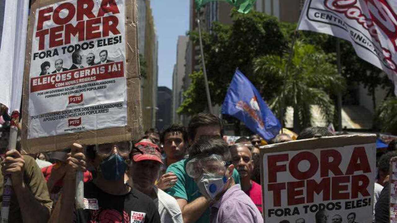 Demonstrators hold signs that read in Portuguese "Temer out. General elections now!" outside the state of Rio de Janeiro's legislative assembly building