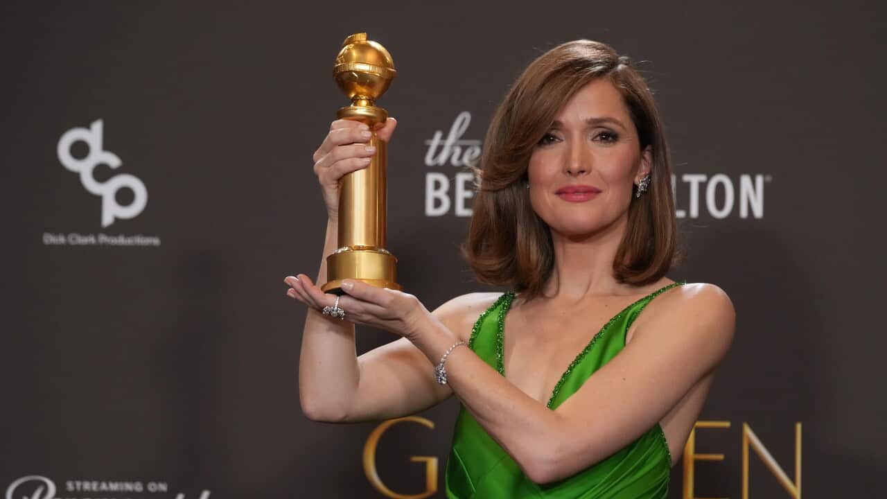 A white woman with brown hair wearing a green dress holding up a golden trophy