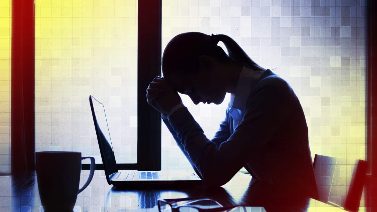 A silhouette of a woman sitting at a computer with her head resting on her fists