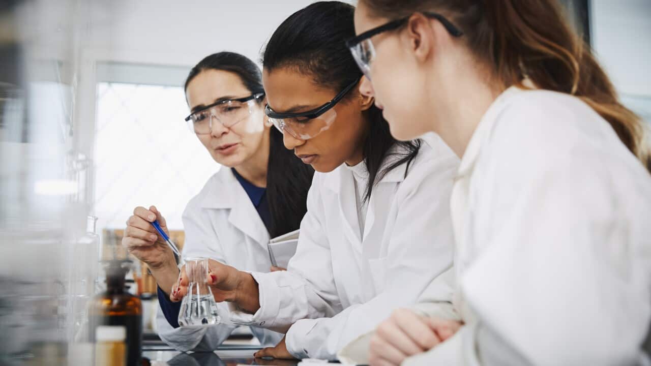 Female chemistry teacher explaining to young multi-ethnic students in laboratory