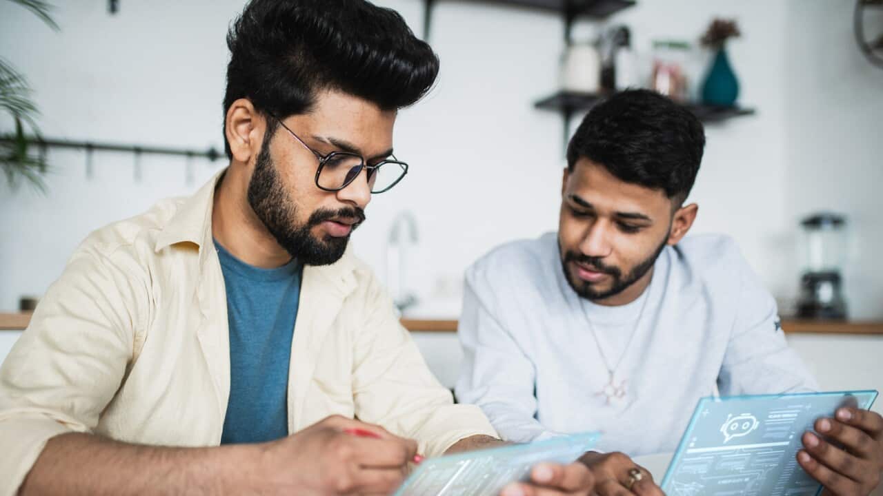 Two Indian men working together on a tablet with digital projection screen with hologram representing technologies of the future. Working on AI Chatbot development and accebility