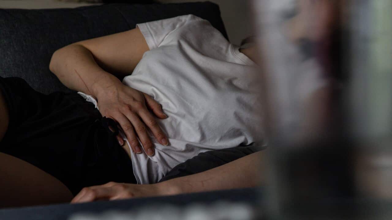A person holds their stomach as they lie on a couch