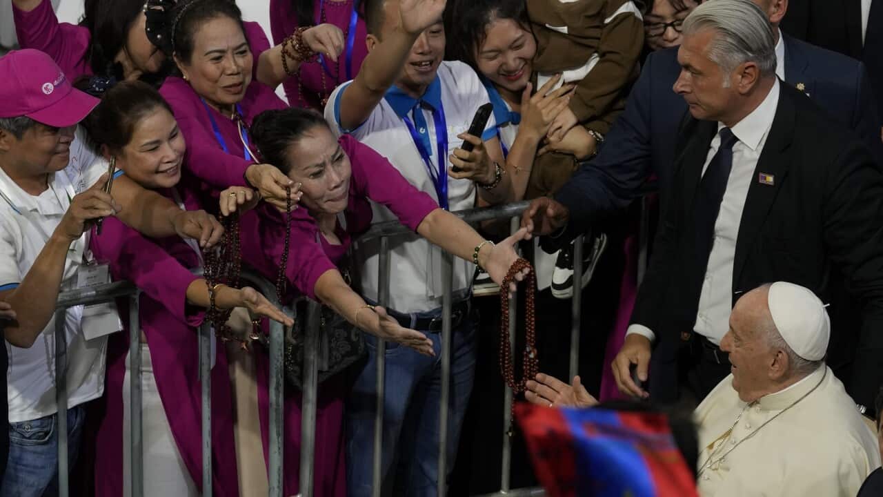 Catholic adherents stretch their arms out towards the Pope with a fence between them.