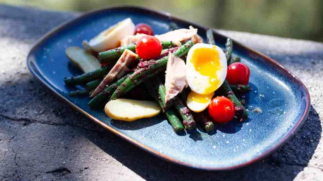 A french and virant salad sits onn a modern rectangular blue plate, on a stone surface.