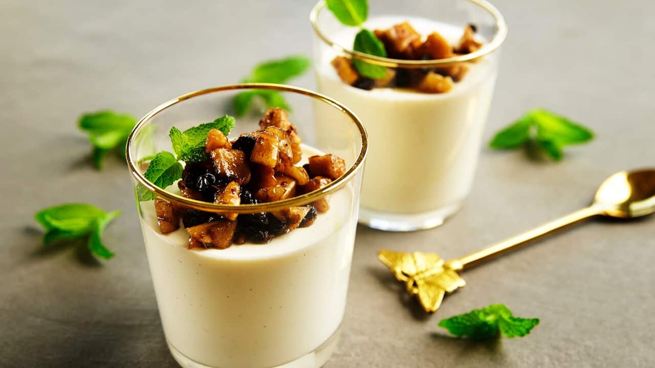 Two glasses are filled with a creamy mixture, with a golden-brown topping. A fancy gold spoon sits beside the glasses.