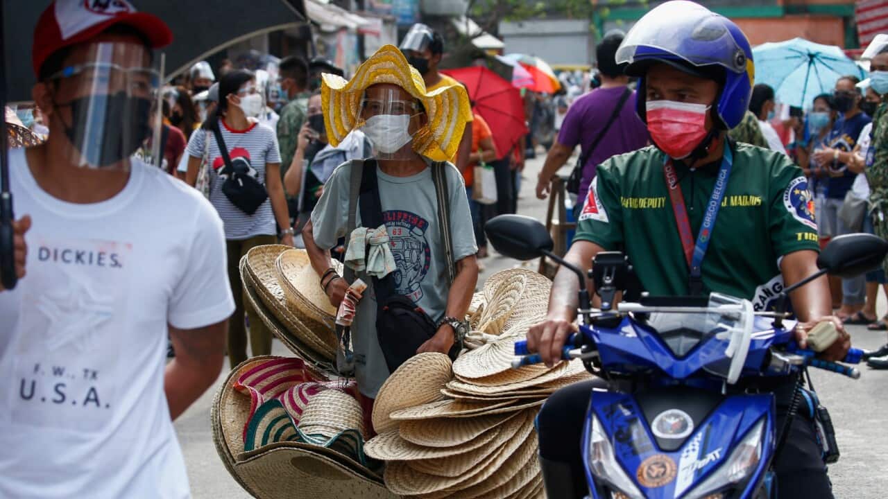 A fan vendor (C) walks past citizens queueing to receive financial aid as part of a government program for families affected by the COVID-19 lockdown measures