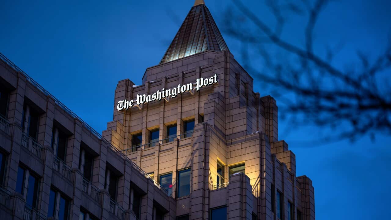 A nighttime shot of a building, topped with a tower-like roof and an illuminated “The Washington Post“ logo.