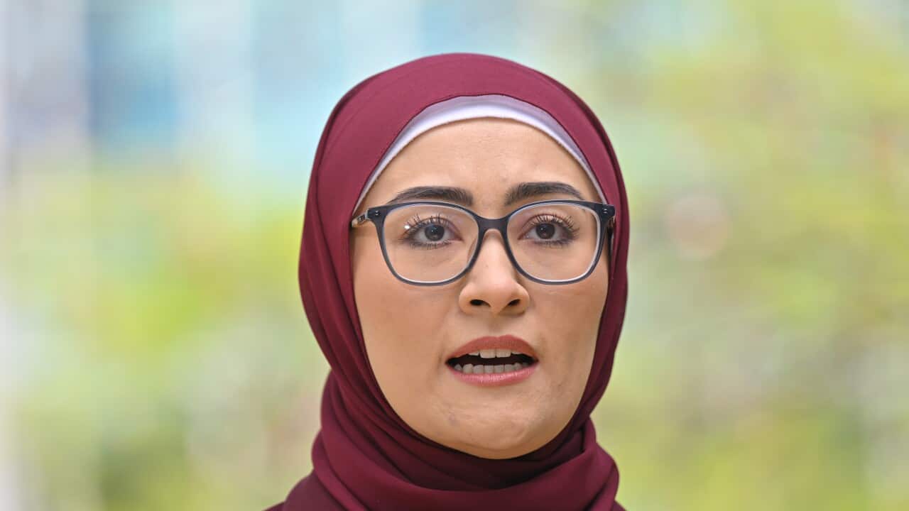 A woman wearing glasses speaking while standing outside.