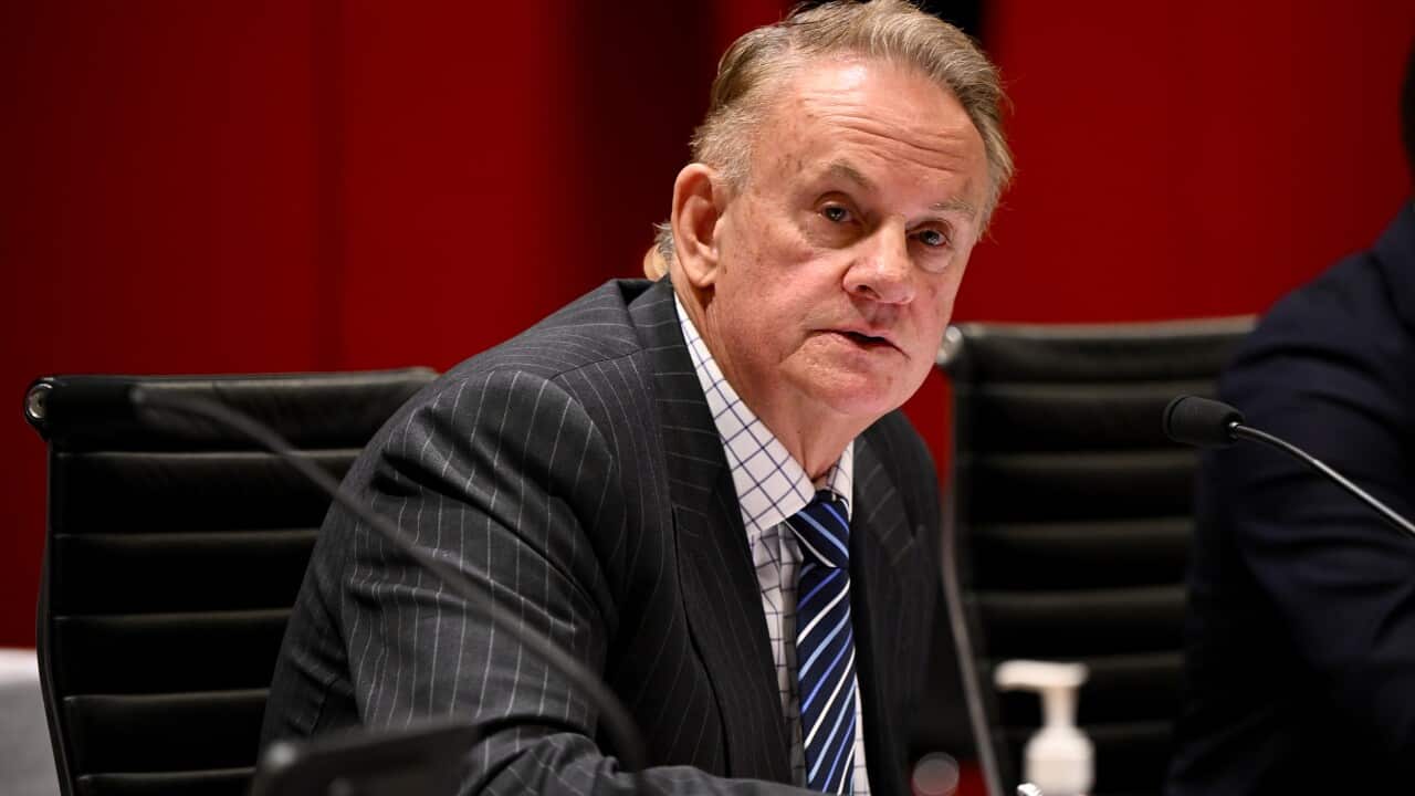 A man in a black pinstripe suit, sitting at a desk with papers in front of him.