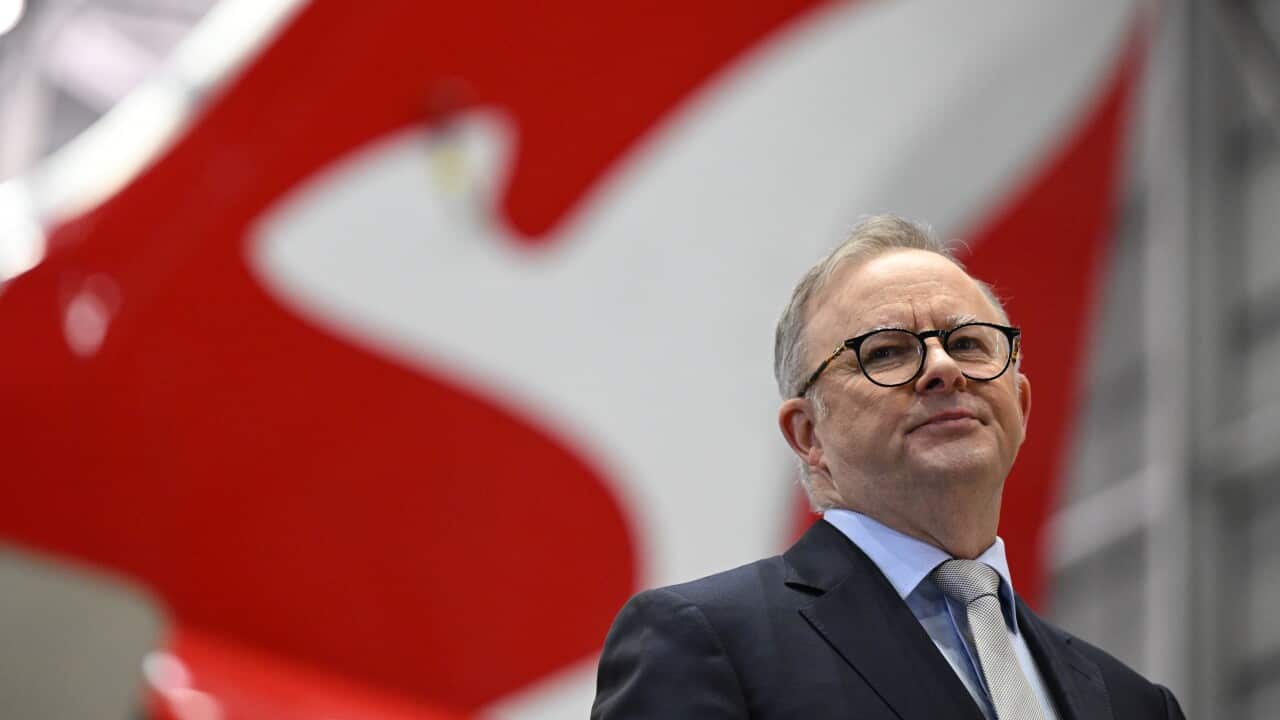 Anthony Albanese (centre) stands flanked by a woman and a man against a red background featuring Qantas logos.