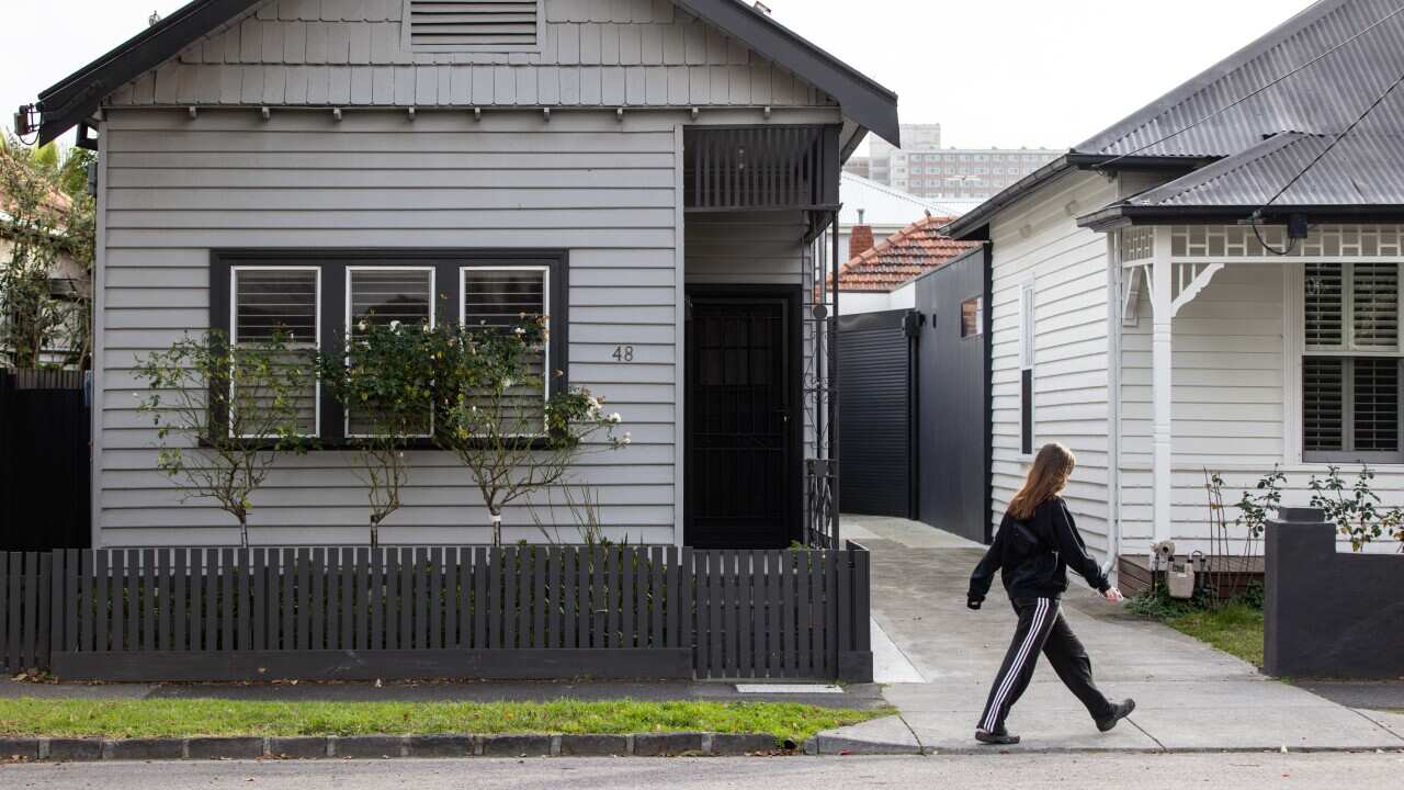 A woman walking in front of a grey house with a dark grey fence.