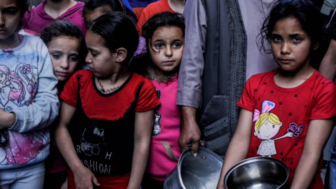 Palestinian girls seen with dishes waiting for prepared food distributed in Shajaiya neighbourhood during Ramadan